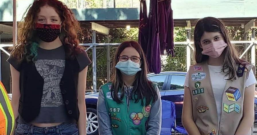 Three girlscouts  with mask on looking forward outside with black car in background